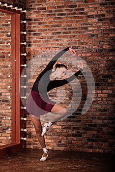 Beautiful young female classical ballet dancer on pointe shoes wearing a black leotard and skirt on a brick background