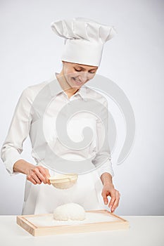 Beautiful young female cook powdering dough with flour