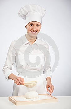 Beautiful young female cook powdering dough with flour