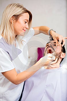 Beautiful young female dentist examining young male patient in dental clinic
