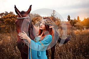 Beautiful young female elf with long dark wavy hair petting her horse resting in the woods forest nymph stroking her horse care