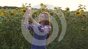 Beautiful, young, female farmer holding a bottle of sunflower oil, in the middle of a sunflower field