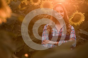 Beautiful, young female farmer smiling in the middle of a sunflower field during sunrise