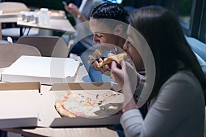 Beautiful young female friends woman eating pizza and drinking cola while sitting inside expres restaurant late at night