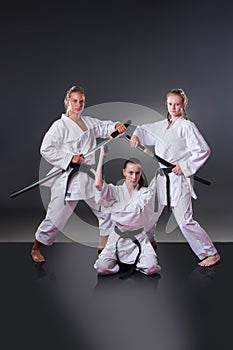 Beautiful young female karate players posing with sword on the gray background