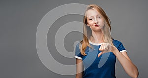 Beautiful young female looking is upset at the camera, holding thumb down. Concept of dislike