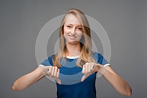 Beautiful young female looking is upset at the camera, holding two thumbs down. Concept of dislike