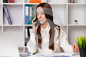 Beautiful young female manager talking on the phone while working on a laptop in the office