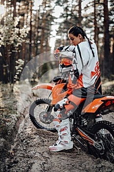 Beautiful young female racer riding motocross bike on a trail of sand in the woods