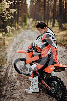 Beautiful young female racer riding motocross bike on a trail of sand in the woods