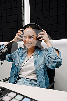 Beautiful young female radio host using microphone and headphones while broadcasting in studio