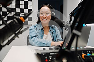 Beautiful young female radio host using microphone and laptop while broadcasting in studio