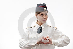 A beautiful young female Russian police officer in dress uniform shows a heart with her hands and smiles on a white background