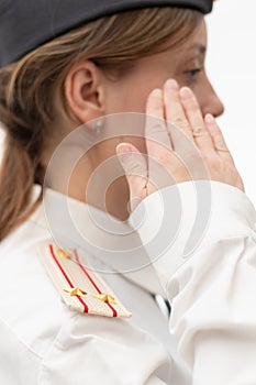 A beautiful young female Russian police officer in dress uniform and a white shirt on a white background salutes the commander.