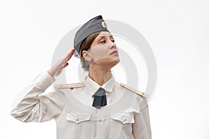 A beautiful young female Russian police officer in dress uniform and a white shirt on a white background salutes the commander.