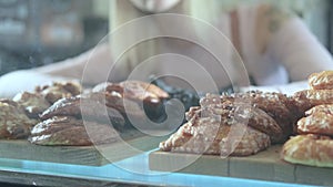 Beautiful young female seller working in the confectionery store. Close-up of fresh pastries on a vitrine