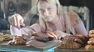 Beautiful young female seller working in the confectionery store. Close-up of fresh pastries on a vitrine