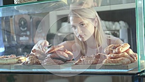 Beautiful young female seller working in the confectionery store. Close-up of fresh pastries on a vitrine