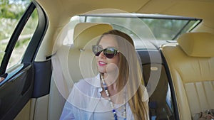 Beautiful young female in sunglasses sitting in elite taxi and enjoying view