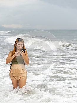 Beautiful young Filipina woman,playfully paddling in the shallow waves of the long sandy beach at Iba,Zambales,Luzon,Philippines