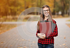 Beautiful young financial businesswoman in glasses looking at camera and smiling while standing in park after business meeting