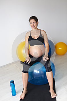 Beautiful, young, fit, athletic and pregnant woman with black hair doing fitness exercises in a modern apartment