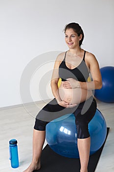 Beautiful, young, fit, athletic and pregnant woman with black hair doing fitness exercises in a modern apartment