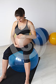 Beautiful, young, fit, athletic and pregnant woman with black hair doing fitness exercises in a modern apartment