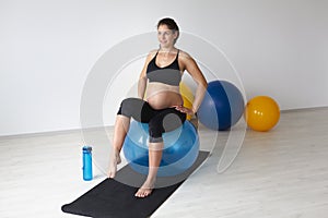 Beautiful, young, fit, athletic and pregnant woman with black hair doing fitness exercises in a modern apartment