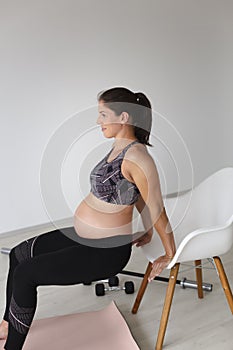 Beautiful, young, fit, athletic and pregnant woman with black hair doing fitness exercises in a modern apartment