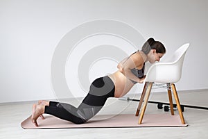 Beautiful, young, fit, athletic and pregnant woman with black hair doing fitness exercises in a modern apartment