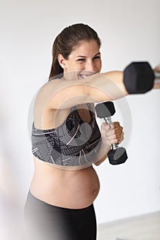 Beautiful, young, fit, athletic and pregnant woman with black hair doing fitness exercises in a modern apartment