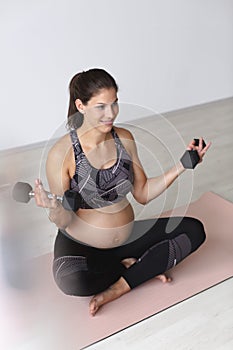 Beautiful, young, fit, athletic and pregnant woman with black hair doing fitness exercises in a modern apartment