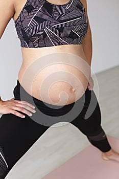 Beautiful, young, fit, athletic and pregnant woman with black hair doing fitness exercises in a modern apartment