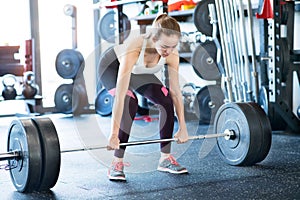 Beautiful young fit woman in gym lifting heavy barbell