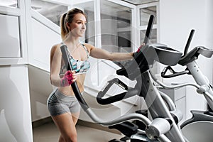 Beautiful young fitness woman at the gym exercising on the xtrainer machines. Attractive fit model doing cardio. Fat