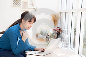 Beautiful young freelance asian woman smiling working and on laptop computer at desk coffee shop with professional