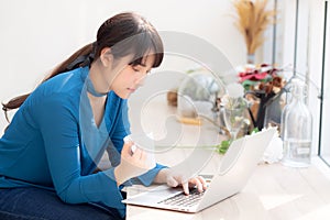 Beautiful young freelance asian woman smiling working and on laptop computer at desk coffee shop with professional