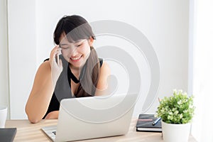 Beautiful young freelance asian woman smiling working on laptop computer and talking mobile smart phone