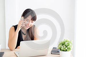 Beautiful young freelance asian woman smiling working on laptop computer and talking mobile smart phone at desk office