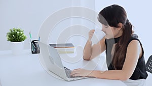 Beautiful young freelance asian woman working on laptop computer drinking coffee when sleepy and yawning at the office