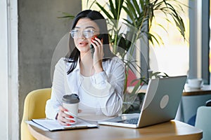 Beautiful Young Freelancer Woman Using Laptop Computer Sitting At Cafe Table. Happy Smiling Girl Working Online Or