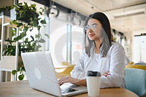 Beautiful Young Freelancer Woman Using Laptop Computer Sitting At Cafe Table. Happy Smiling Girl Working Online Or
