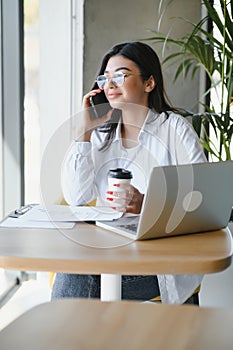 Beautiful Young Freelancer Woman Using Laptop Computer Sitting At Cafe Table. Happy Smiling Girl Working Online Or