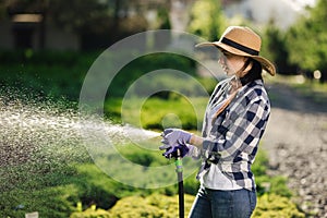 Beautiful young gardener woman watering garden in hot summer day