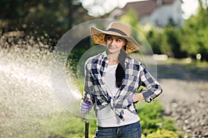 Beautiful young gardener woman watering garden in hot summer day