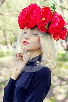 Beautiful young gentle elegant young blond woman with a red crown of peony in a black blouse walks in the lush apple orchard