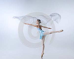 Beautiful young girl, aspiring ballerina in blue dress and pointes dancing with cloth  on gray background. Art