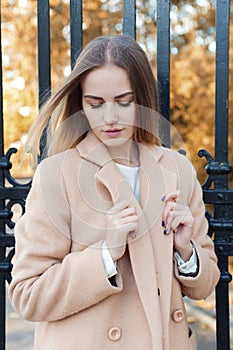 Beautiful young girl in the autumn foliage walks through the city streets on a sunny afternoon in a coat and a warm jacket