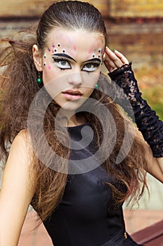 Beautiful young girl on the background of the leaves in autumn day on the street with fantasy makeup in a black dress